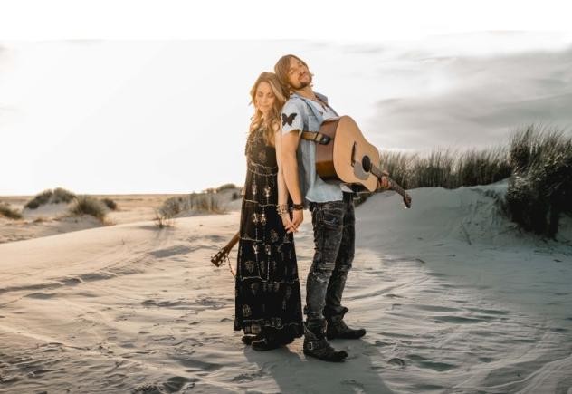 Mann und Frau stehend im Sand mit Gitarre